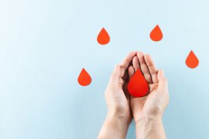 Hands of caucasian woman cupping blood drop, with blood drops on blue background, copy space