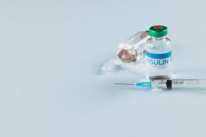 Vials of insulin with caplets and syringe on blue background with copy space